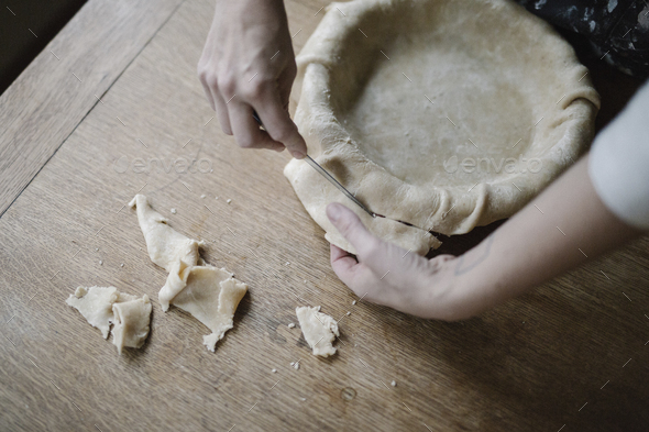 A woman using raw pastry dough to line a pie dish and finish the edge.