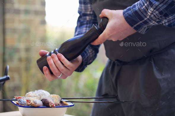 A spatchcocked game bird being seasoned for cooking, a man\'s hand grinding pepper in a mill.