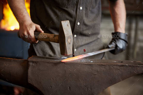 An artisan metal worker shaping a red hot piece of metal on an anvil.