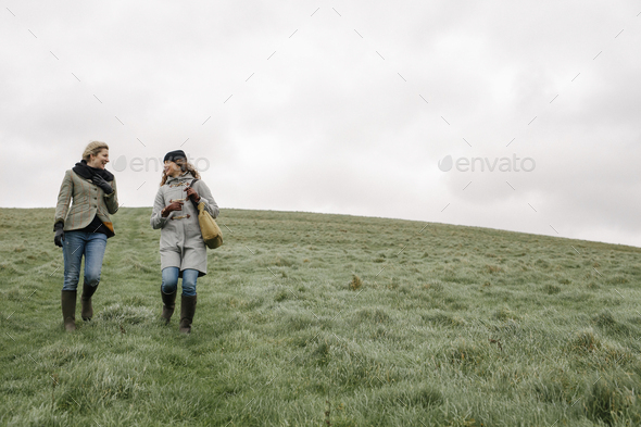 Two women walking across grass. - Stock Photo - Images