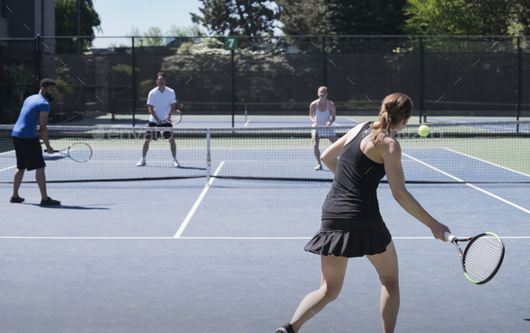 Four people playing tennis on outdoors court, a woman playing a forehand shot.