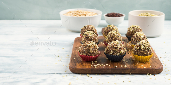 Home made vegan energy protein balls with oats, nuts, dates, dried fruit, flax and hemp seeds, chocolate nibs and maple syrup served in paper cases on wooden board. Copy space, banner