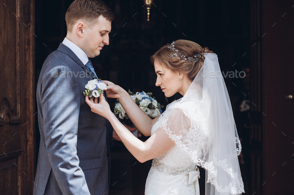 Іlonde bride putting on boutonniere on handsome groom