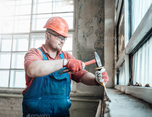 Builder at a construction site working on a windowsill with a hammer
