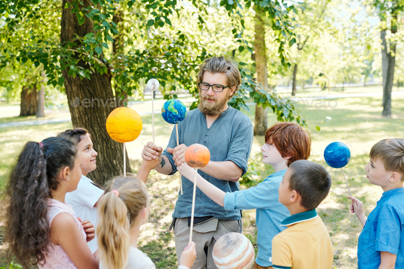 Young bearded teacher in eyeglasses working with group of elementary students at outdoor astronomy lesson
