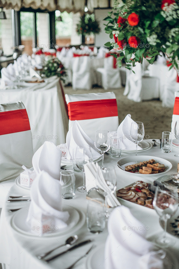 Wedding table with food, silver cutlery, empty glasses, white silk chairs and napkins