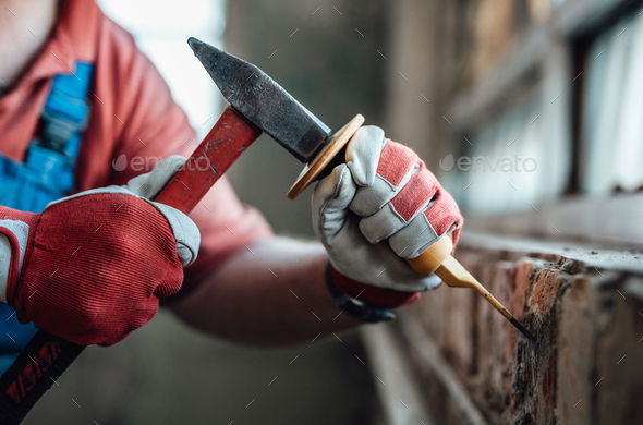 Worker's strong hands with hammer and chisel, getting rid of plaster on a brick wall