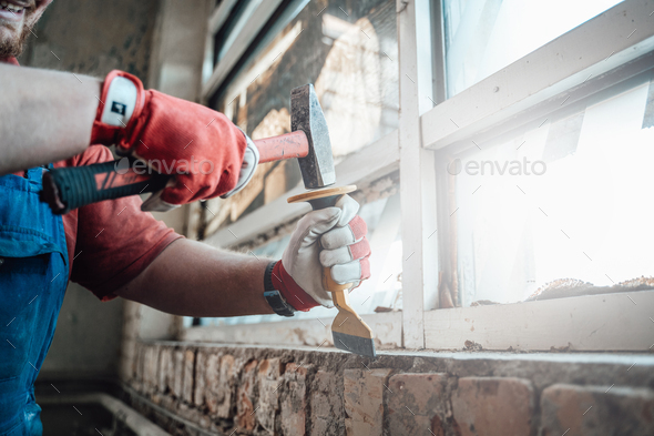 Worker\'s strong hands with hammer and chisel, getting rid of plaster on a brick wall