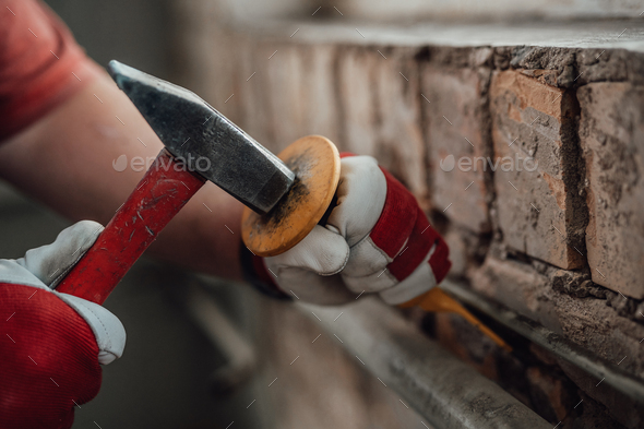 Builder\'s gloved hands working with hammer and chisel at the construction site