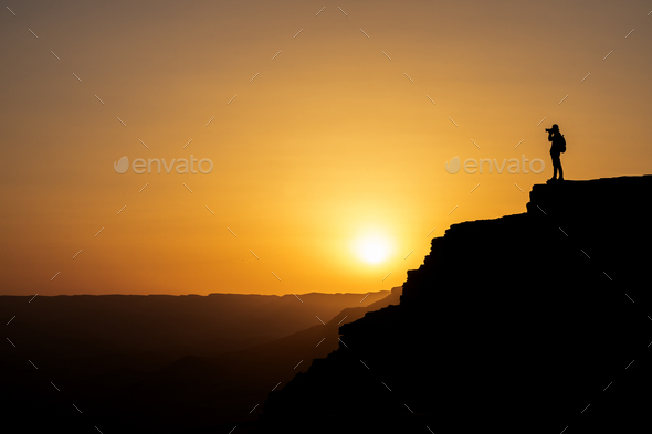 Silhouette of a unrecognizable photographer who shoots a sunset in the mountains. Photographer concept