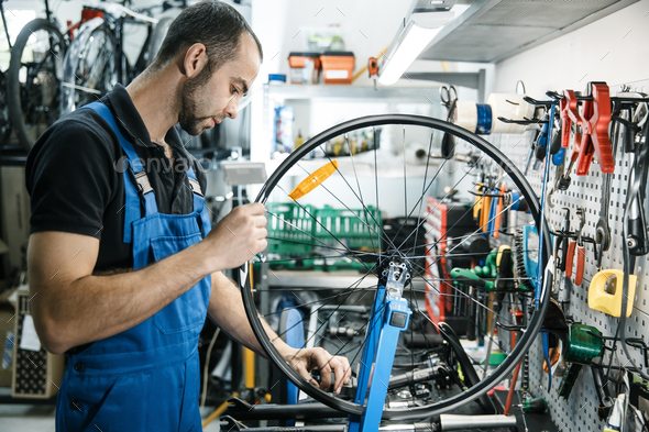 Bicycle repair in workshop, man works with wheel. Mechanic in uniform fix problems with cycle, professional bike repairing service