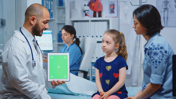 Doctor and patients looking at green screen tablet in medical office. Healthcare specialist with chroma key notebook isolated mockup replacement screen. Easy keying medicine medical related theme.