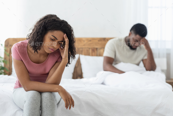 Young married african american couple having relationships crisis, sad man and woman sitting on bed apart. Upset black man and woman after fight, thinking about divorce or breaking up, home interior