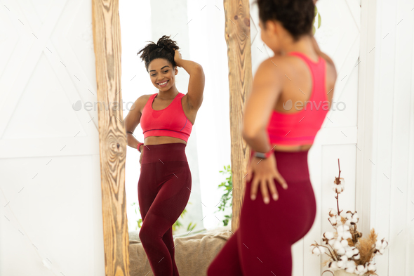 Joyful Fit Black Lady After Successful Weight Loss Posing Near Mirror Looking At Reflection Standing At Home. Weight-Loss, Slimming Motivation Concept. Selective Focus