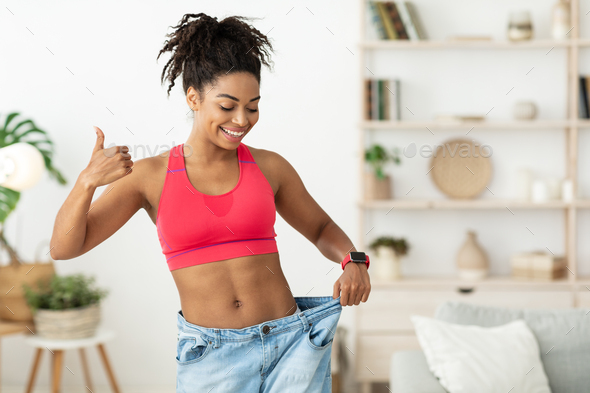 African Lady Gesturing Thumbs-Up Wearing Oversize Jeans After Slimming Indoor