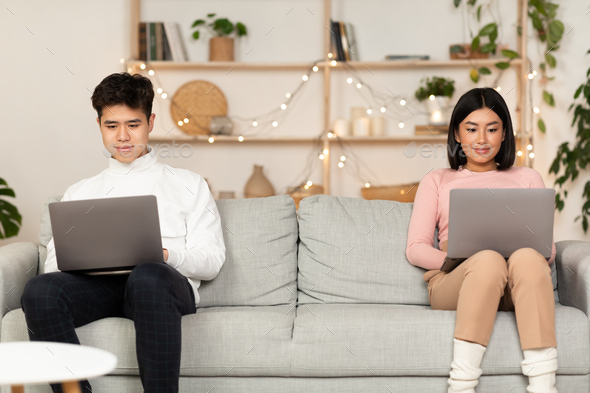 Korean Couple Using Laptop Computers Sitting On Couch At Home On Weekend Evening. Online Relationship Concept, Internet Websites And Family Web Life. Free Space For Text