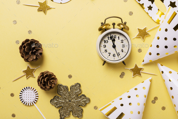 Christmas card with party hats, masks and clock on the yellow background. Top down view with copy space