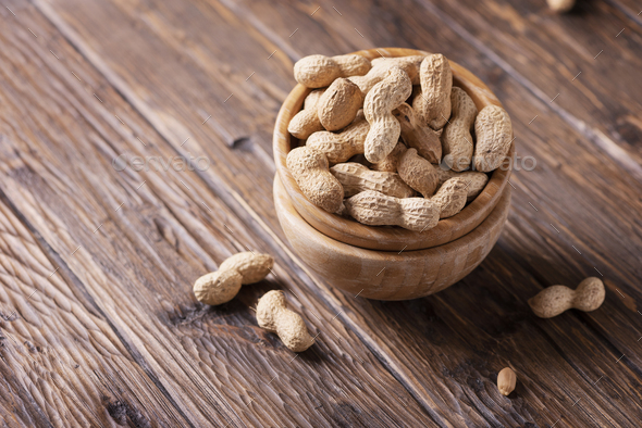  Roasted peanuts in wooden bowl on dark background, selective focus image