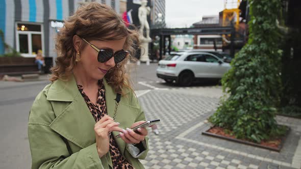 Young Stylish Woman Looking at Smartphone Screen While Standing Outdoors