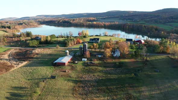 Aerial Drone Shot Orbiting a Lakeside Farm with Silos and Fall Colors alt
