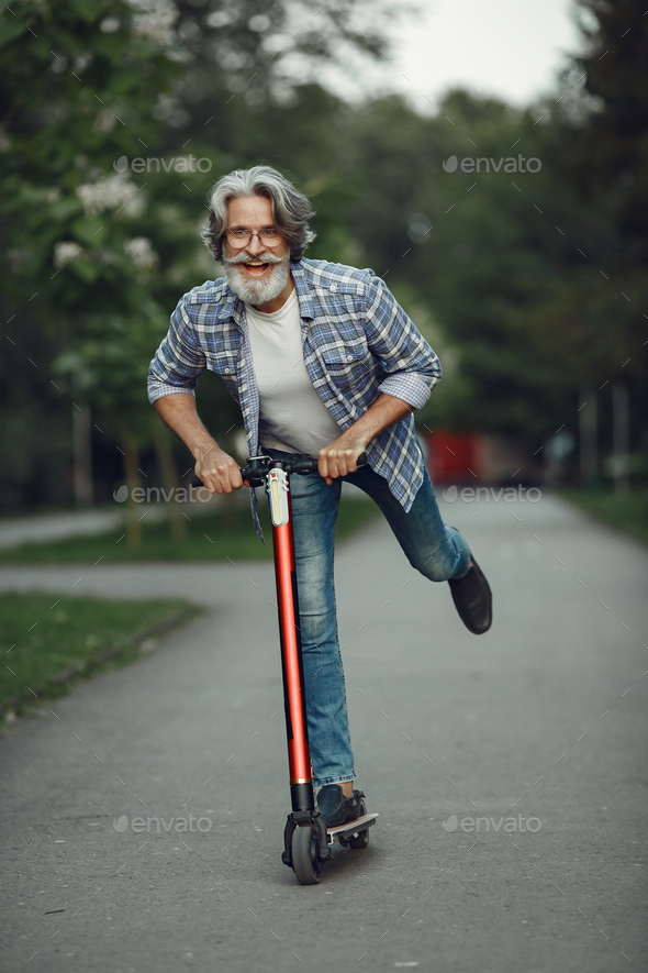 Portrait of elderly man with kick scooter in a summer park