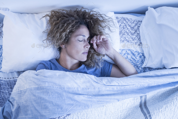 Beautiful adult caucasian lonely woman sleep alone in a double bed at home – concept of independence and portrait of people sleeping and relaxing – morning wake up concept
