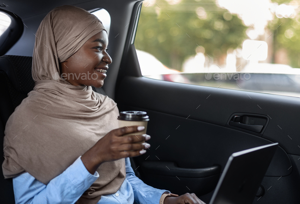 Cheerful Black Muslim Lady In Hijab Drinking Takeaway Coffee In Car
