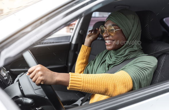 First Car. Cheerful Young Black Muslim Woman In Hijab Driving New Auto