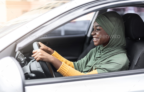 Muslim female driver. Smiling black islamic woman in hijab driving her car