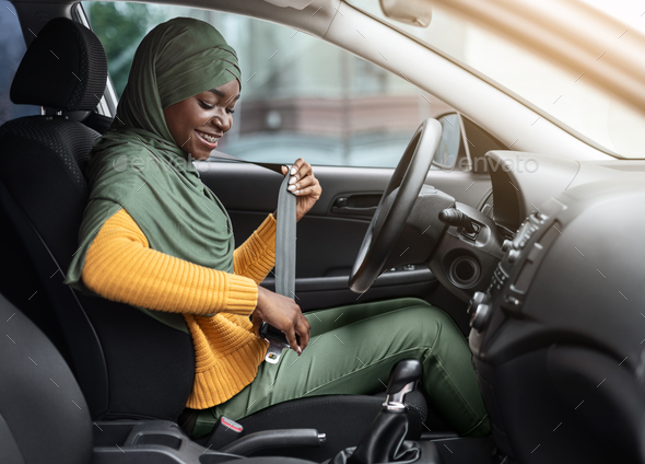 Safety First. Smiling Black Muslim Woman In Hijab Fastening Seatbelt In Her Car Before Driving In City, Following Safe Ride Rules, Ready For Travel With Auto, Side View With Free Space