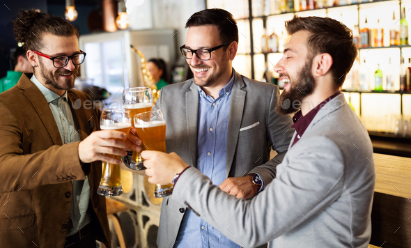 Happy business people drink beer after work in pub. Businessmen enjoy a beer.