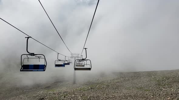 Clouds Enveloping Modern Ropeway with Benches in Amazing Mountainous Terrain alt