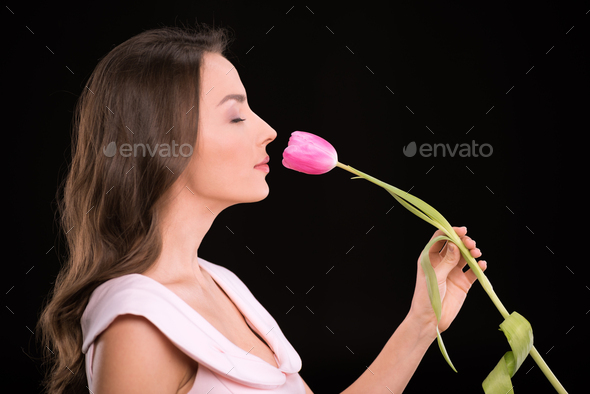 Side view of beautiful young woman with closed eyes smelling tulip flower isolated on black,