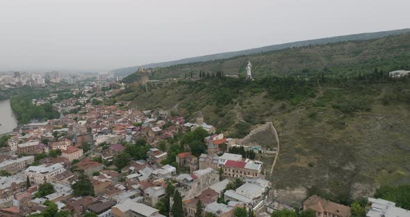 Slow aerial shot of the Old Tbilisi neighborhood and Kartlis Deda in the back. alt