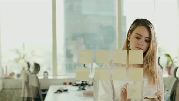 young businesswoman sticking sticky notes on glass at office alt