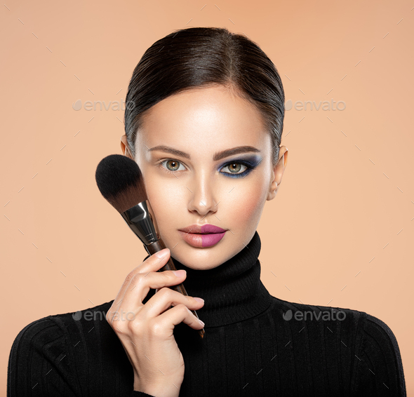 Portrait of a girl with cosmetic brush near face. Woman making makeup on the face using makeup brush. One half face of a beautiful white woman with bright makeup and the other is natural.
