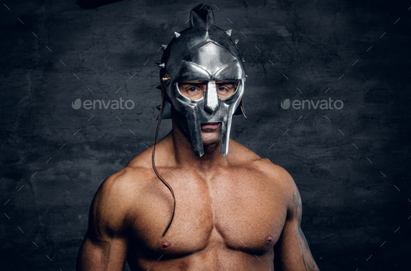 Brutal shirtless muscular male in a gladiator silver helmet on grey background.