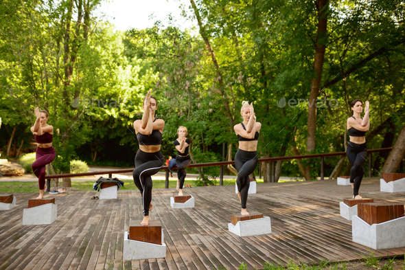 Slim women doing balance exercise on group yoga training in summer park. Meditation, fit class on workout outdoors, relaxation practice. Fitness, active healthy lifestyle