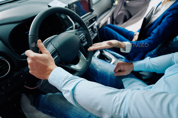 Cropped image of car dealership manager sitting in car compartment with customer and showing advantages of new model