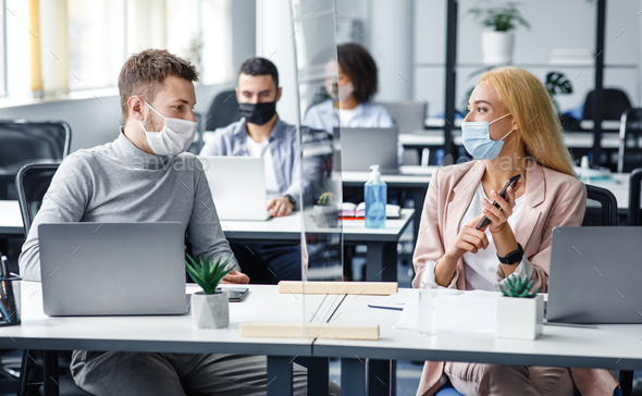 Man and woman in protective masks maintain social distance at work. Employees discuss work sitting