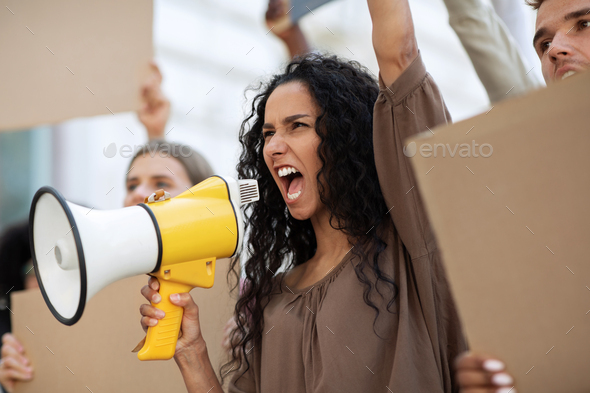 Active mixed race woman with megaphone leading public meeting on the street. International group of young people holding empty placards, protesting against discrimination or racism, closeup