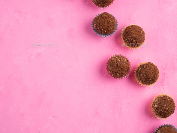 Home made vegan energy protein balls with oats, nuts, almond butter, dates, dried fruit, flax seeds, chocolate nibs in colorful paper cases on pink wooden background. Top view, copy space