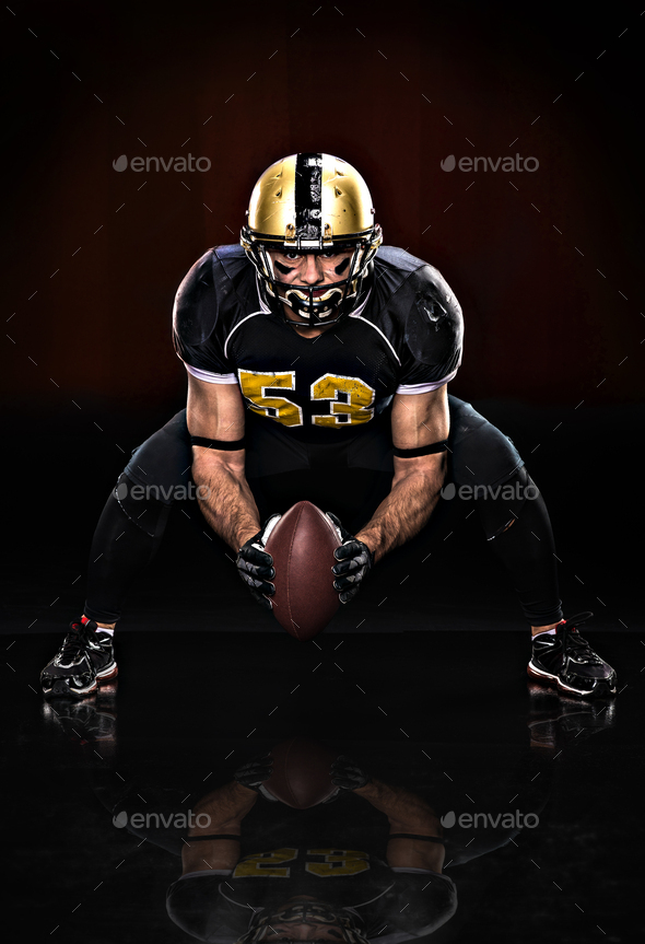 American football player in protective sportswear holding ball on dark