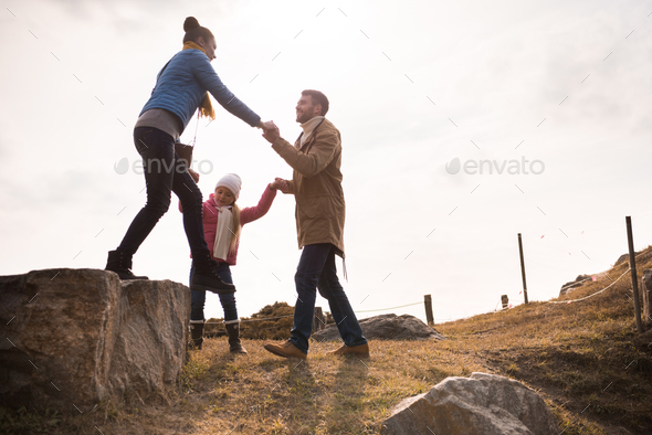 Happy family holding hands and walking on big stones on meadow at sunny autumn day