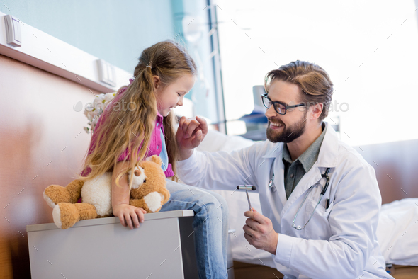 Smiling male doctor using reflex hammer while examining little patient
