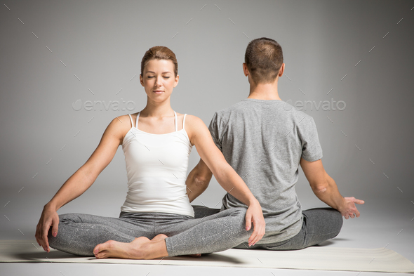 Young couple practicing yoga sitting in lotus position on yoga mats isolated on grey
