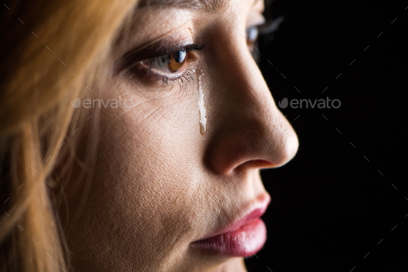 Close-up side view of young woman crying isolated on black