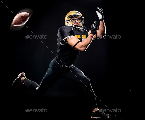 Full length view of american football player in protective sportswear catching ball on black