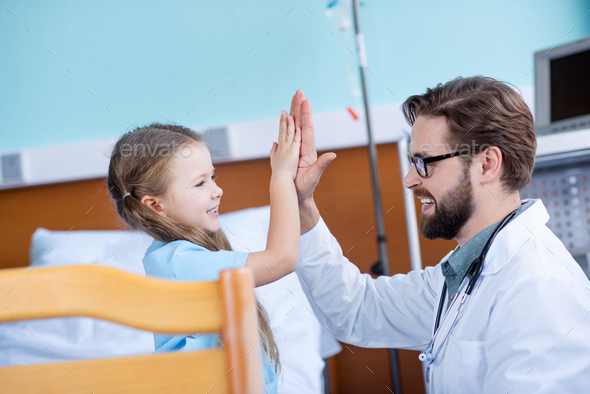 Side view of smiling male doctor and cute little girl giving high