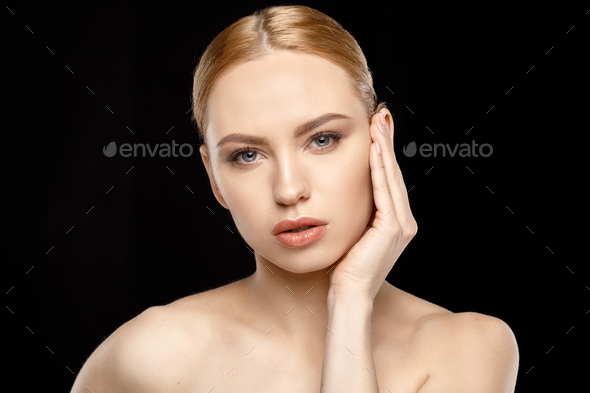 Sensual young blonde woman with hand on face looking at camera isolated on black